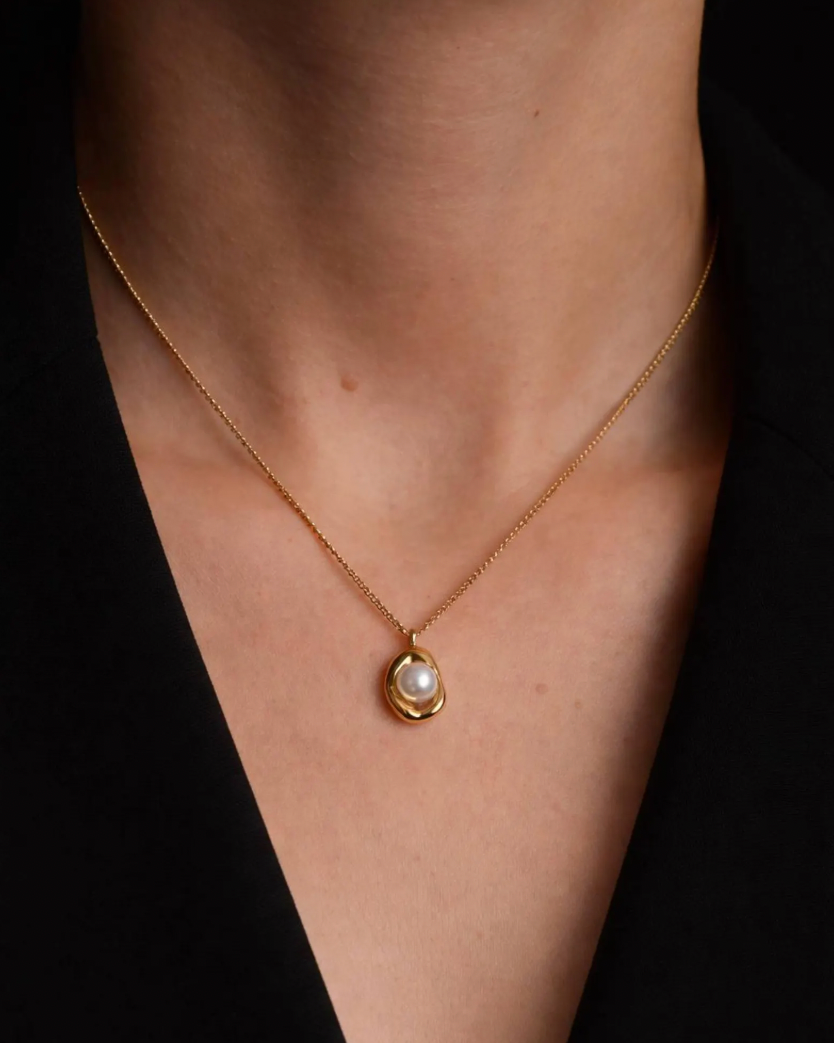 Gold necklace with a pearl pendant on a person's neck against a dark background