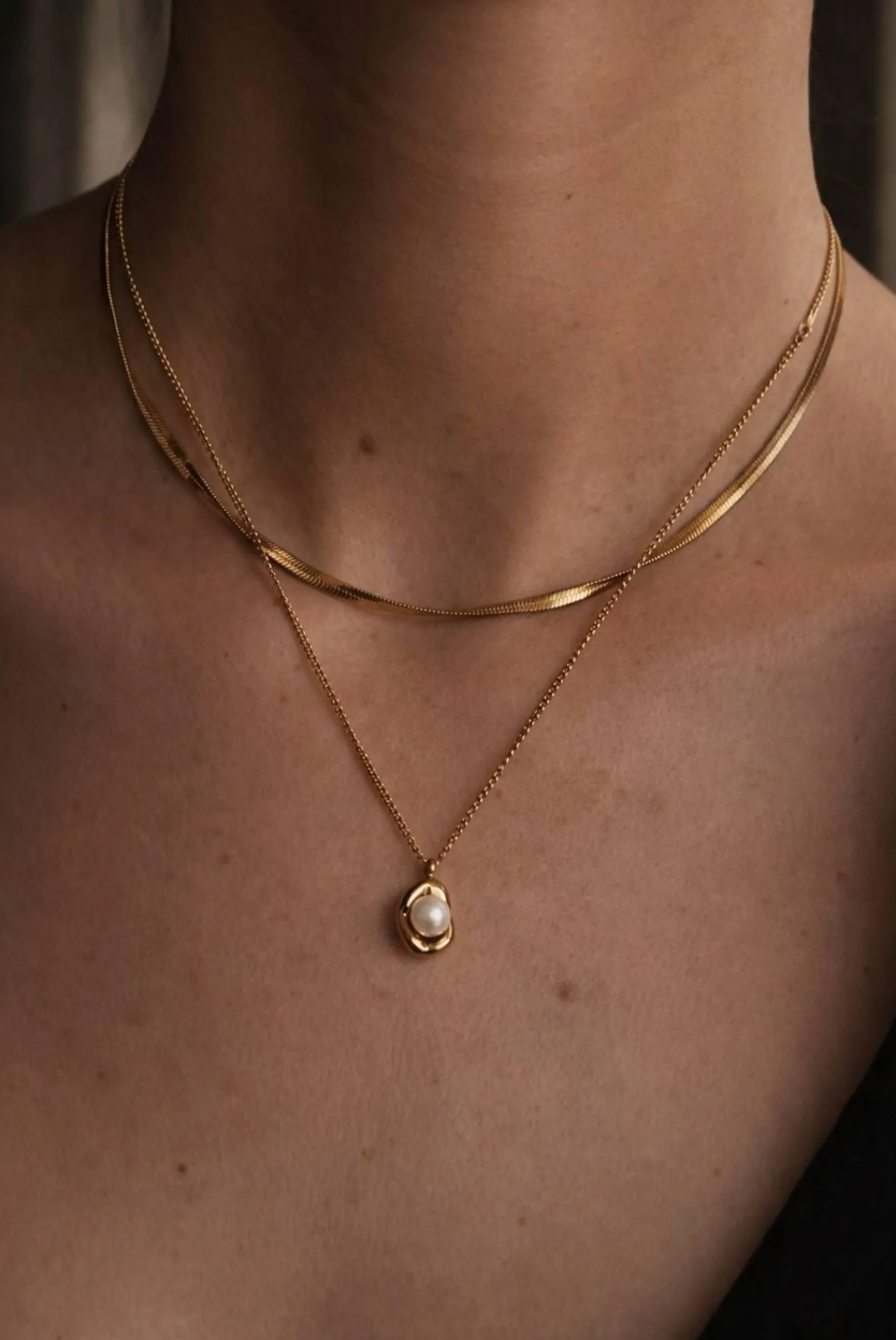 Gold necklace with a pearl pendant on a person's neck against a neutral background