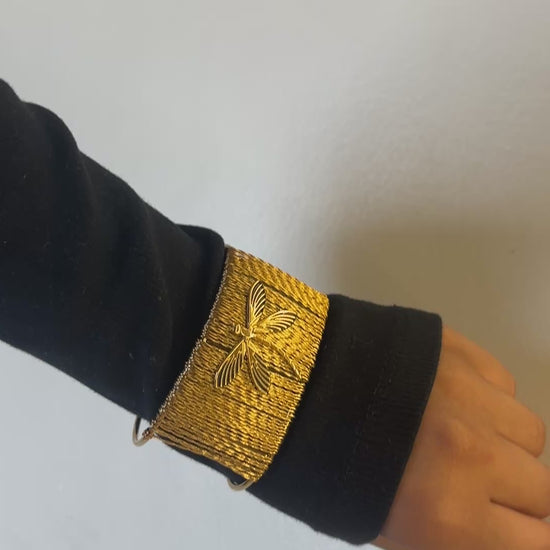 Gold bracelet with a butterfly design on a white background